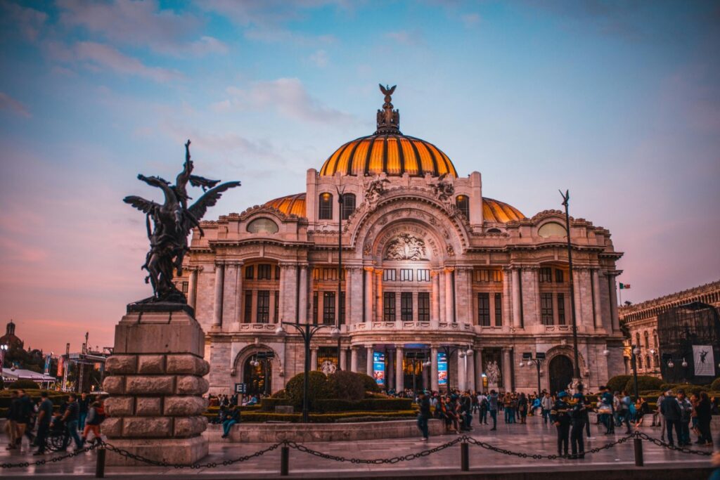 La imponente fachada del Palacio de Bellas Artes en la Ciudad de México, con su icónica cúpula dorada y una estatua imponente al frente. Hay muchas personas en la plaza. Perspectivas del marketing en redes sociales en México para 2025: Este lugar emblemático puede ser una gran fuente de inspiración para campañas de marketing en redes sociales en México el próximo año.