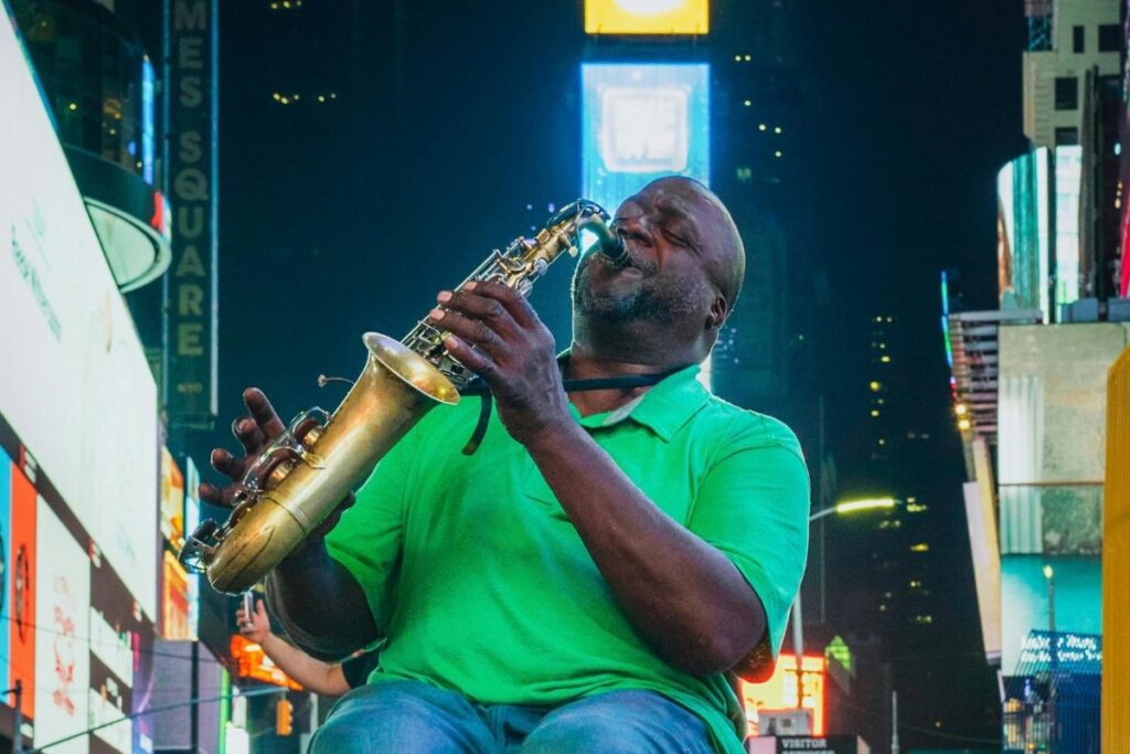 Un músico en un lugar concurrido, vistiendo una camisa verde y tocando un saxo. En el fondo, hay carteleras iluminadas. Sobre BaoLiba – Revolucionando la colaboración entre marcas e influencers en México. Este escena dinámica puede ser una gran oportunidad para las campañas de colaboración entre marcas e influencers impulsadas por BaoLiba.