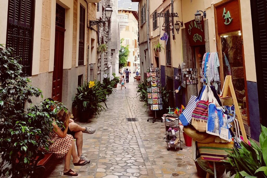 Una encantadora calleja empedrada con edificios a ambos lados. Hay plantas, tiendas con artesanías y gente caminando y descansando. #Tendencias del Marketing en Redes Sociales en España para 2025